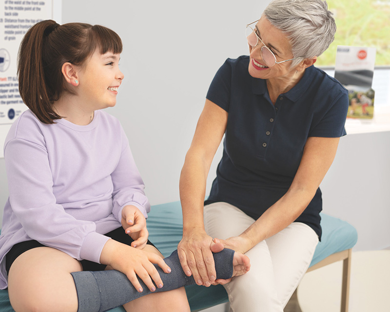 A healthcare professional examines the leg of a young girl who wears a compression garment. A healthcare professional examines the leg of a young girl who wears a compression garment.
